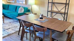 A dining area with a wooden table and chairs, a black metal shelf, and a teal sofa in the background. - 3 Bedroom Townhome in Osoyoos with lake views! XI (Osoyoos)
