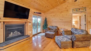 A log cabin interior with a fireplace, a television mounted on the wall, and a Christmas tree.