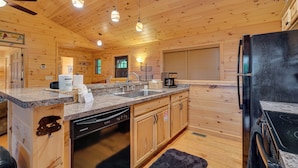 A wooden cabin interior with a kitchen featuring granite countertops, a dishwasher, a refrigerator, and a stove.