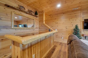 A wooden cabin interior with a wooden counter, a large mirror, a small Christmas tree, and a brown couch. - Private Hot Tub: Gatlinburg Cabin in the Clouds (Gatlinburg)