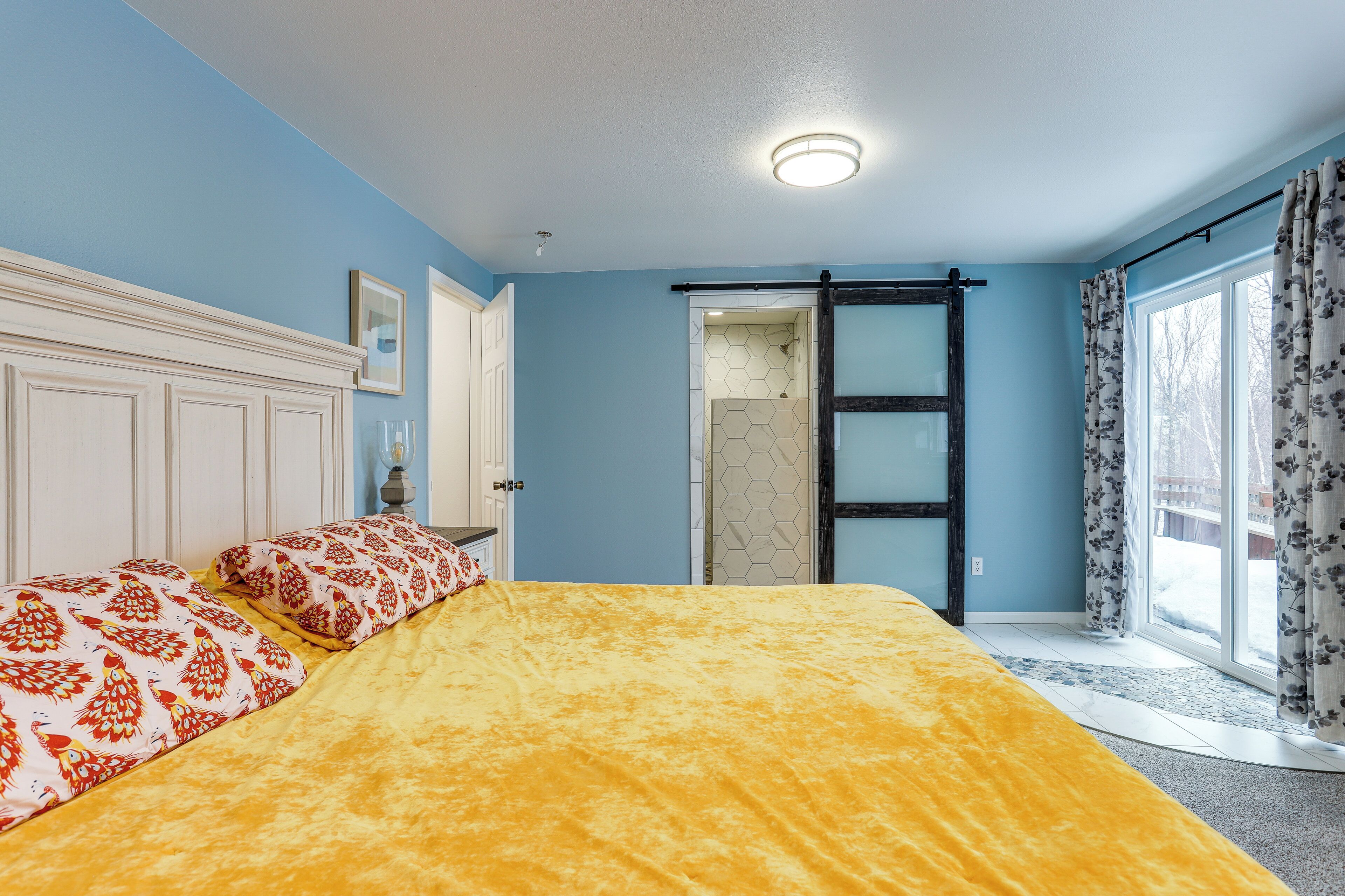 A bedroom with a bed, a door, and a window with curtains.