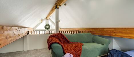 A cozy attic bedroom with a green sofa, a wooden ceiling, and a small window with a wreath.
