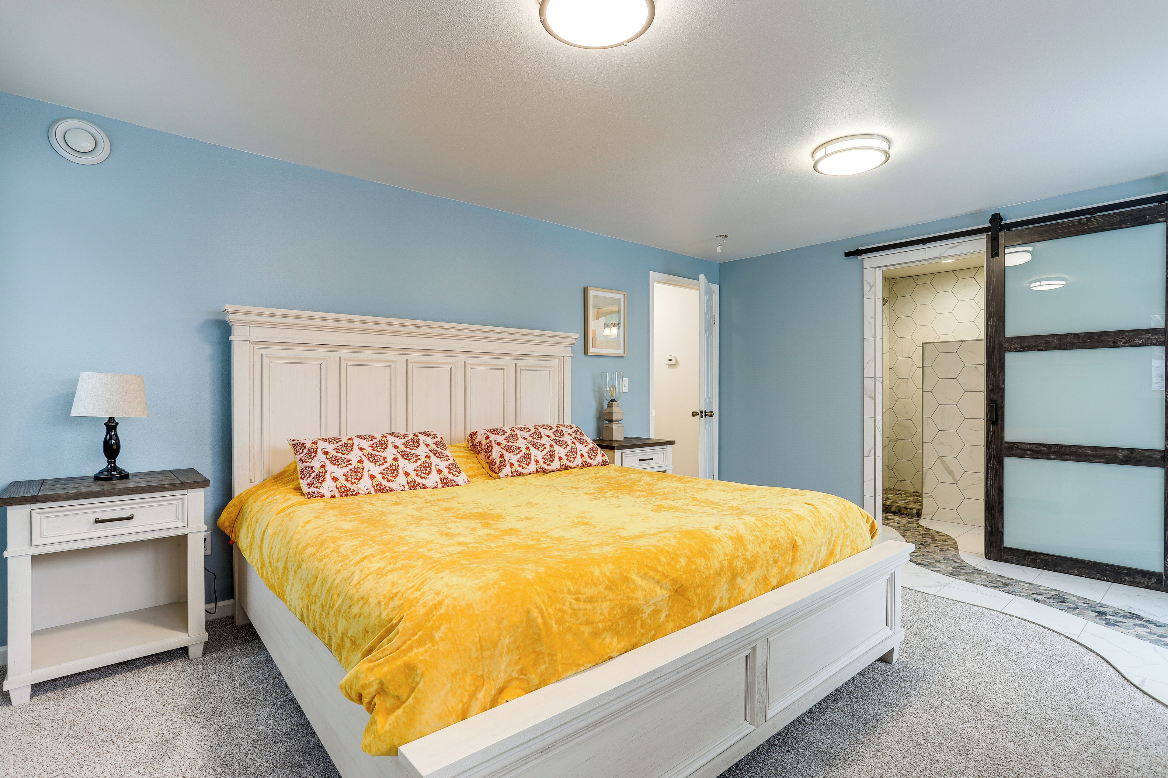 A bedroom with a bed, nightstands, a lamp, and a door leading to a bathroom.