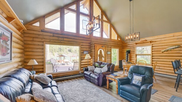 A log cabin interior with a leather sofa, a leather armchair, a dining table with chairs, and large windows. - Soldotna Fishing Lodges w/ Dock on Kenai River! (Soldotna)