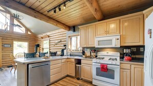 A log cabin-style kitchen with wooden cabinets, a stainless steel dishwasher, a white stove, and a microwave. - Soldotna Fishing Lodges w/ Dock on Kenai River! (Soldotna)