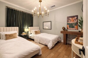 A hotel room with two beds, a chandelier, a painting, and a plant. - Baton Rouge Game Day House w/ Chic Yard Space (Baton Rouge)