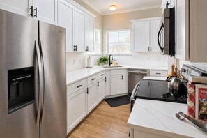 A modern kitchen with stainless steel appliances, white cabinetry, and a black stove. - Baton Rouge Game Day House w/ Chic Yard Space (Baton Rouge)