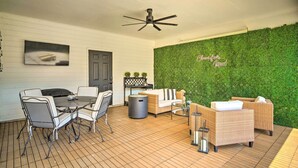 A covered patio with a ceiling fan, a dining table with chairs, wicker sofas, and a green wall with a sign. - Baton Rouge Game Day House w/ Chic Yard Space (Baton Rouge)