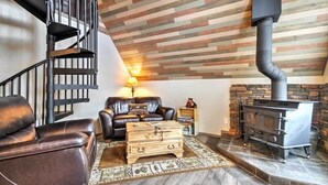 A living room with a fireplace, leather sofa, wooden chest, and a spiral staircase. - Hillside Cripple Creek Cabin w/ Hot Tub, Mtn Views (Cripple Creek)