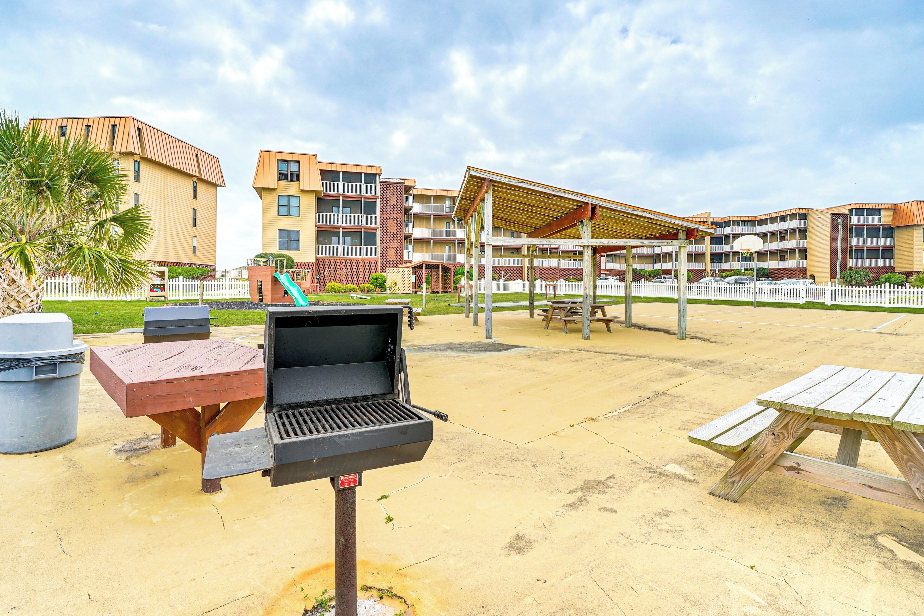 A barbecue grill, picnic table, and a covered seating area in an outdoor setting with a building in the background.
