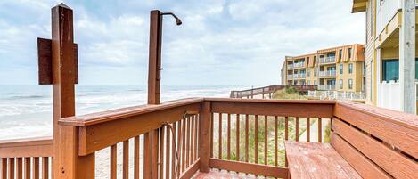 A wooden deck with a bench, a metal railing, and a view of the ocean and buildings in the background.
