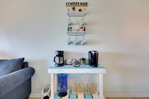 Una cafetería con un letrero que dice 'COFFEE BAR' encima, una máquina de café, un hervidor y una taza de café sobre una mesa azul.