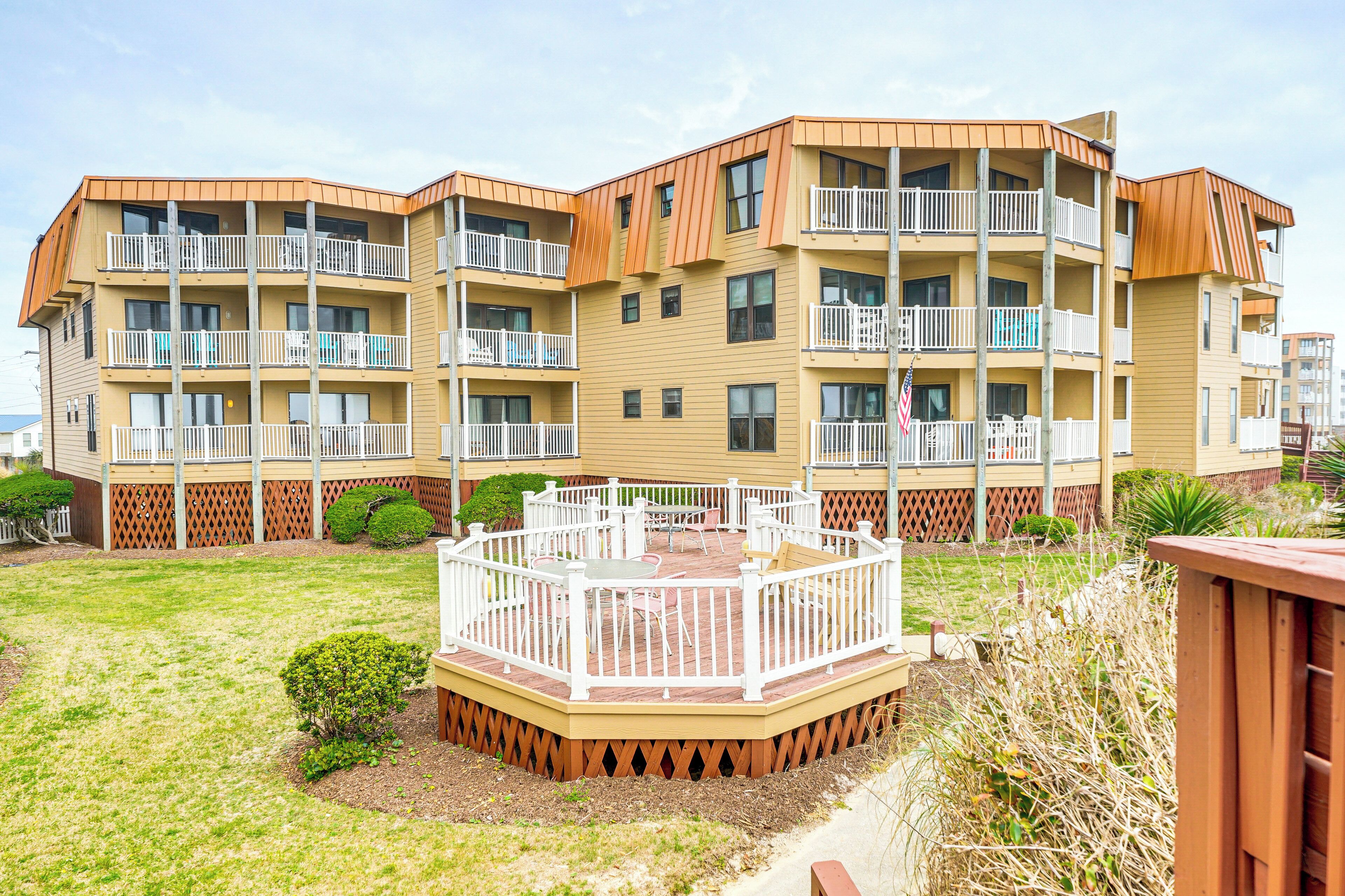 A multi-story residential building with balconies, a deck, and a small garden area.