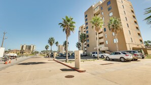 A multi-story building with a parking lot, palm trees, and a clear sky.