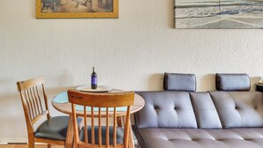 A room with a dining table, chairs, a sofa, and a painting on the wall.