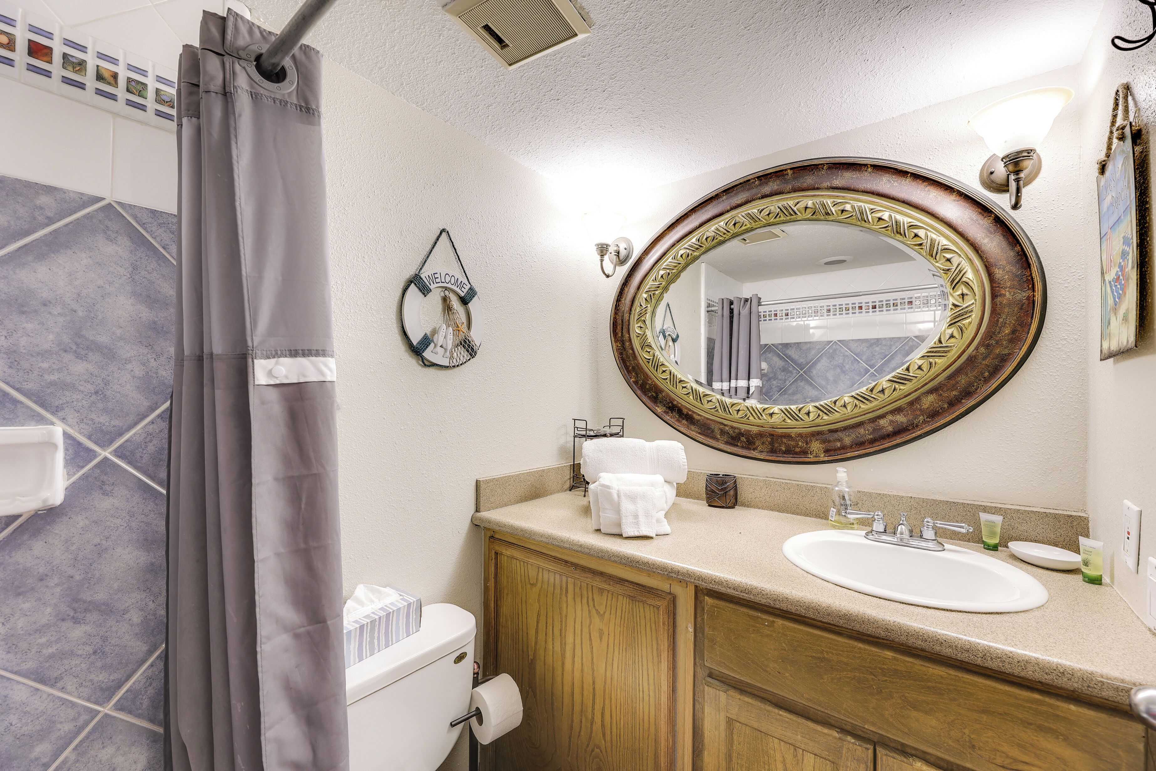 Une salle de bain avec un rideau de douche, des toilettes, un lavabo avec un miroir et un porte-serviettes.