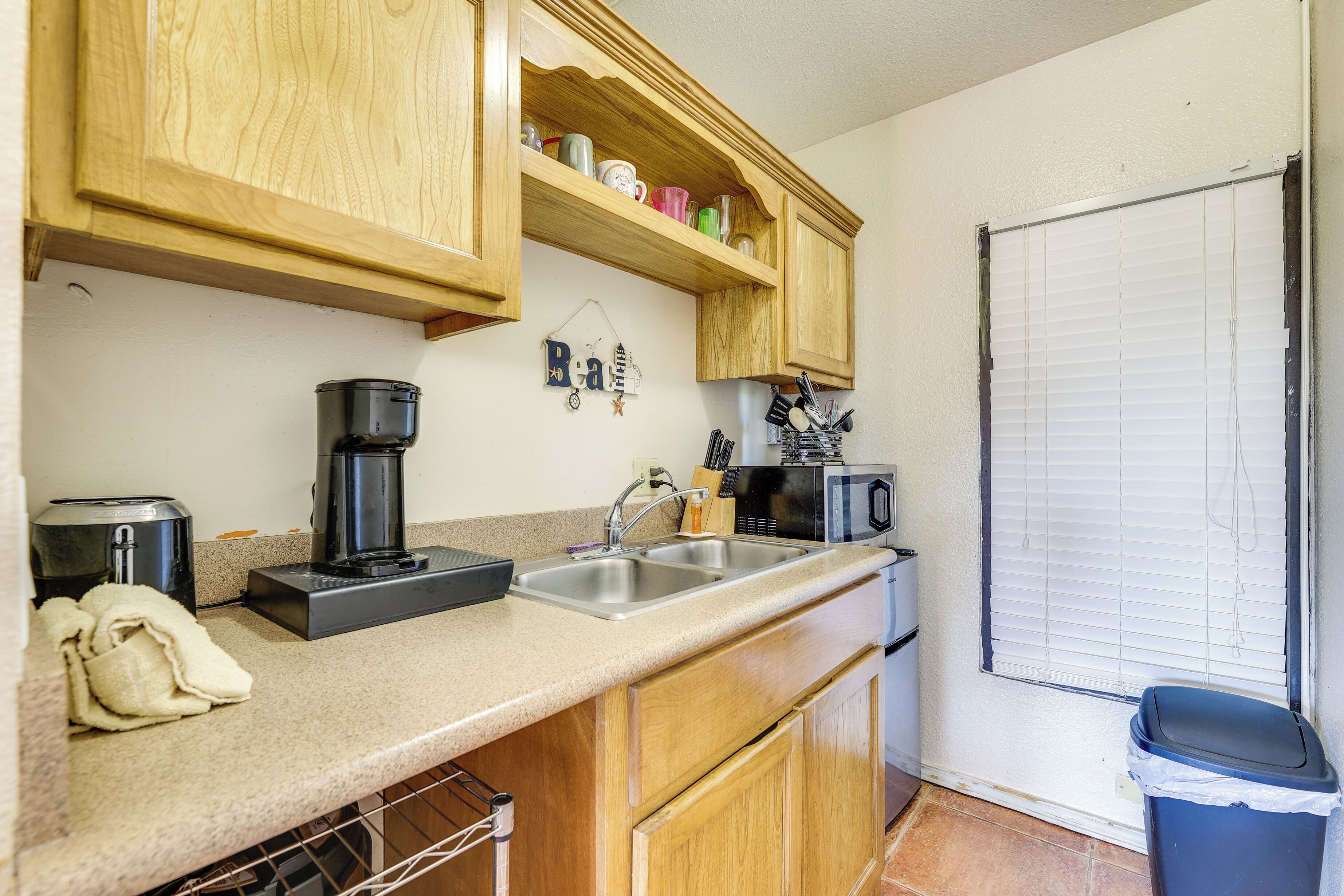 A kitchen with wooden cabinets, a coffee maker, a microwave, and a trash bin.