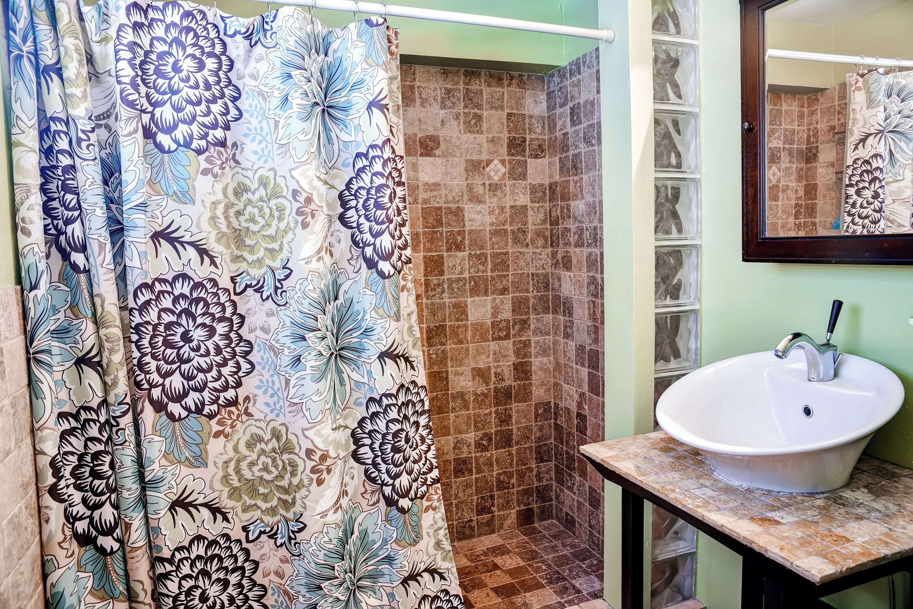 A bathroom with a shower curtain, a sink, and a tiled shower area.