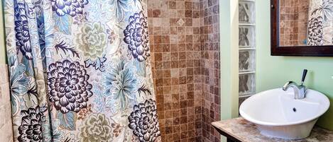 A bathroom with a shower curtain, a sink, and a tiled shower area.