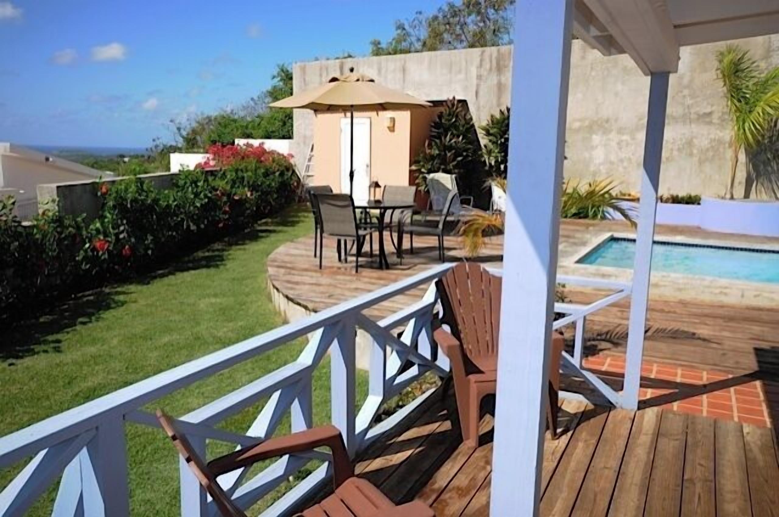 A wooden deck with outdoor furniture, a small building, and a pool.