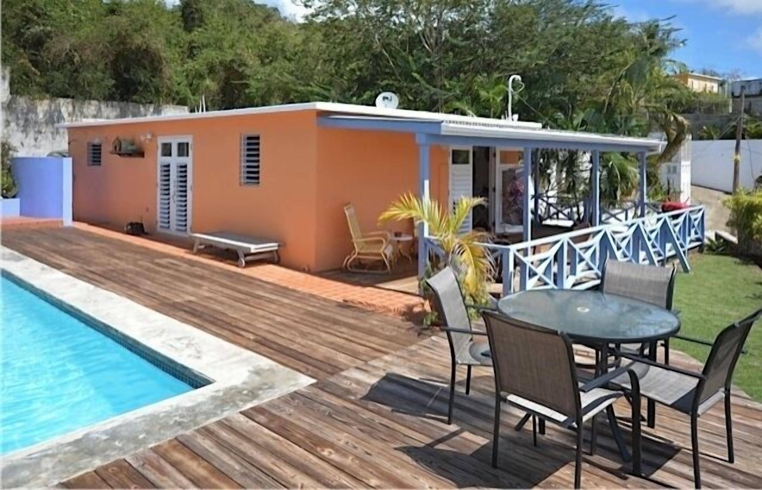 A poolside area with a wooden deck, a small building with a white roof, and outdoor furniture.