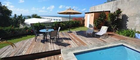 Una terraza de madera con piscina, mobiliario exterior y vista al océano.