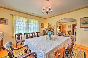 A dining room with a table set for six, surrounded by wooden chairs. A chandelier hangs from the ceiling, and a vase with flowers is on the table.