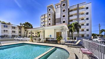A hotel with a swimming pool, outdoor seating, and a white fence.