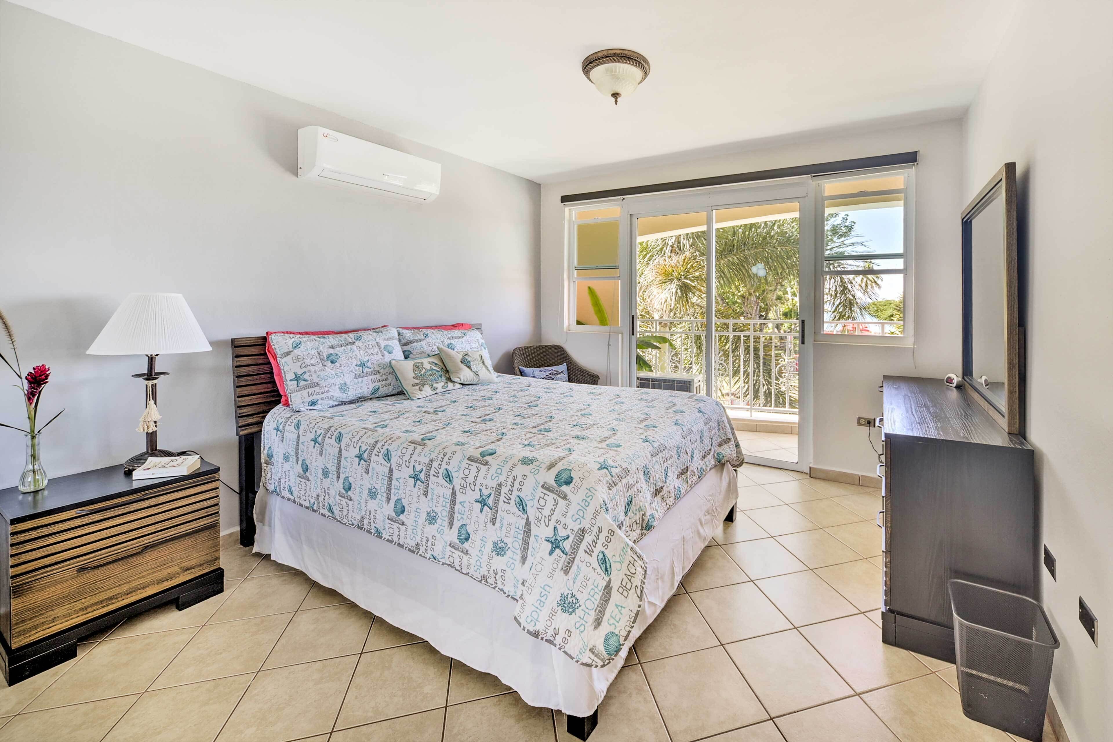 A bedroom with a bed, bedside table, lamp, and a view of the outside balcony.