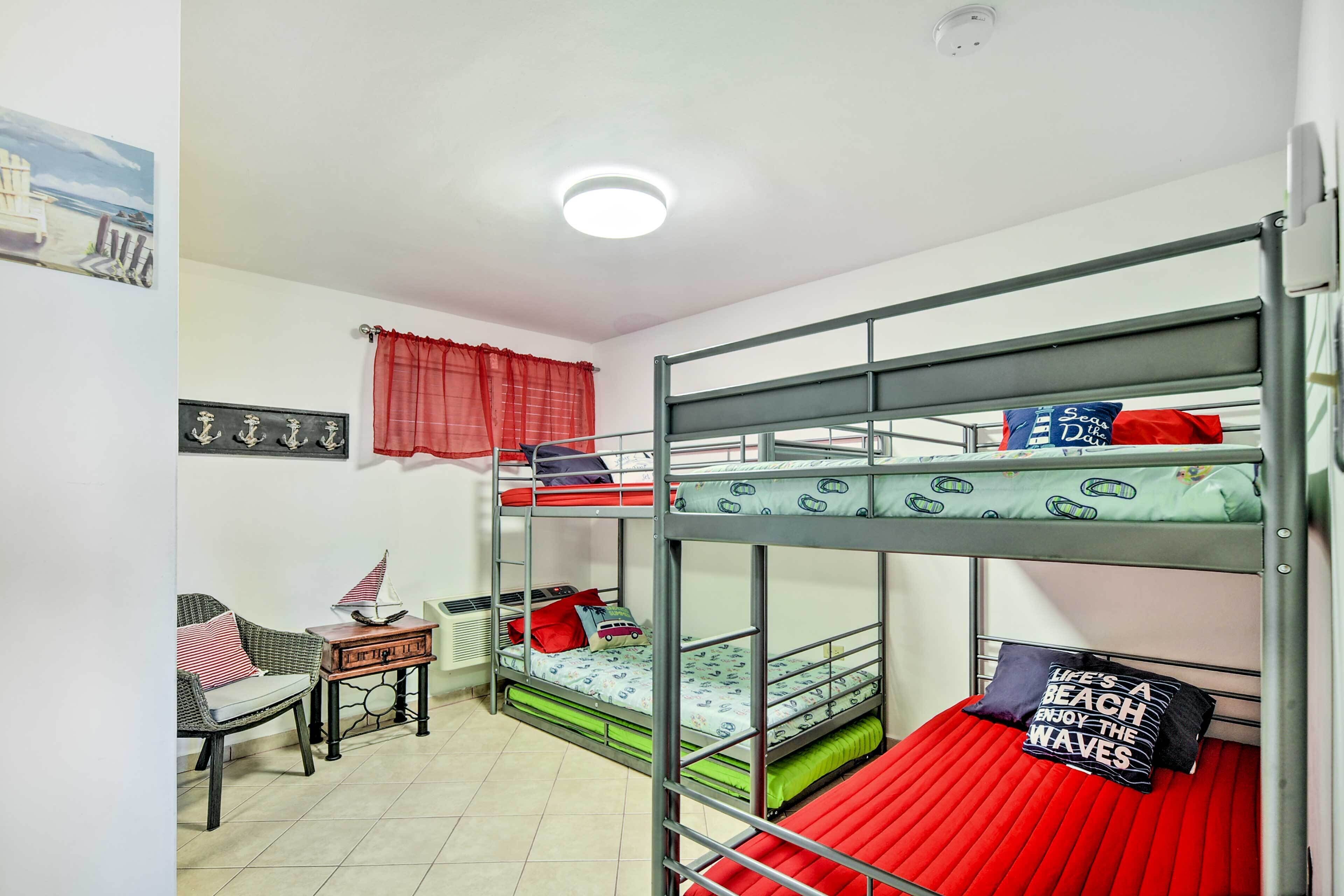 Een slaapkamer met een stapelbed, een rode matras, een klein tafeltje met een lamp en een stoel.