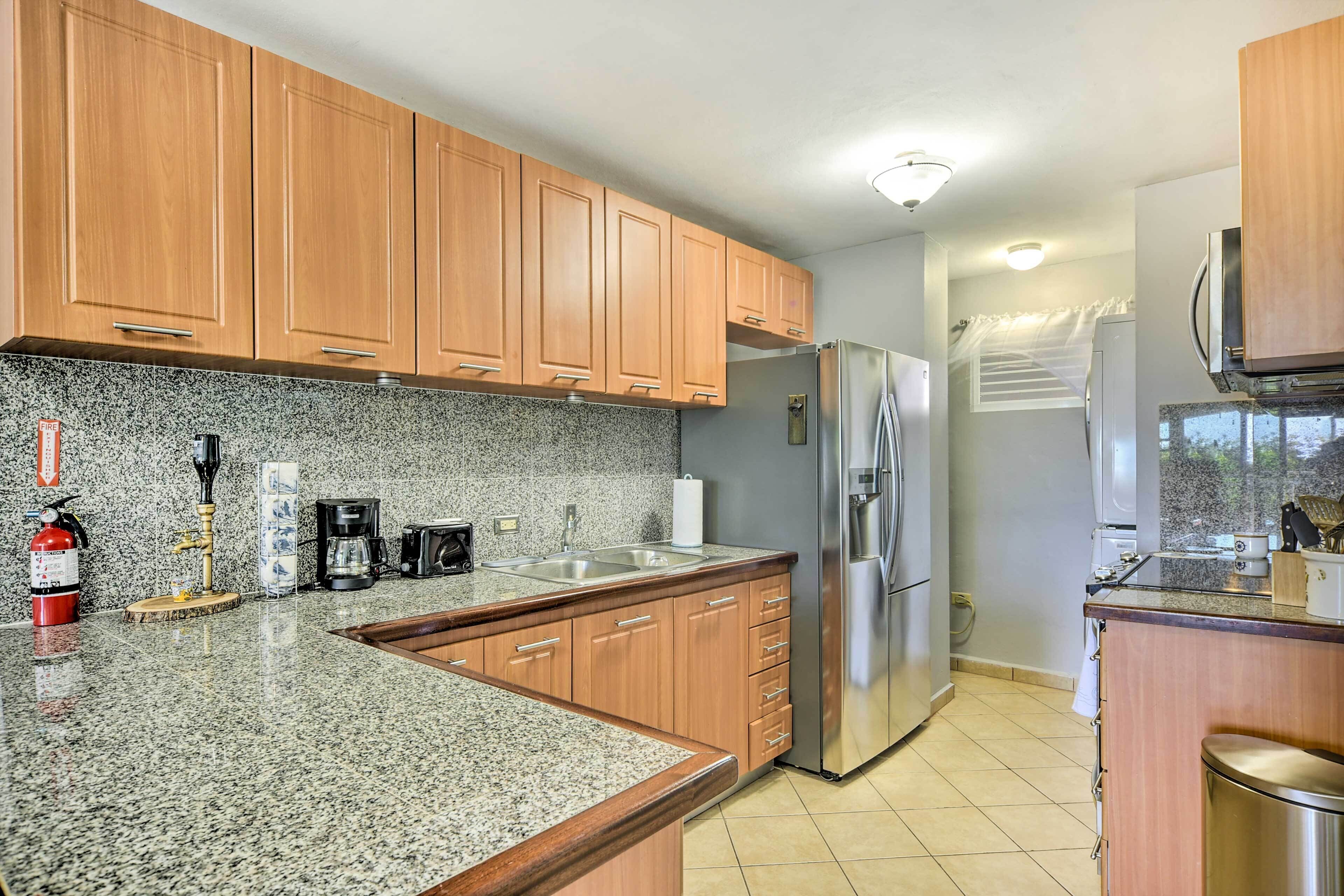 A kitchen with granite countertops, wooden cabinets, stainless steel appliances, and a tiled floor.