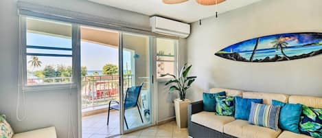 Ein Wohnzimmer mit Sofa, Deckenventilator, Schiebetür und einem an der Wand befestigten Surfbrett.