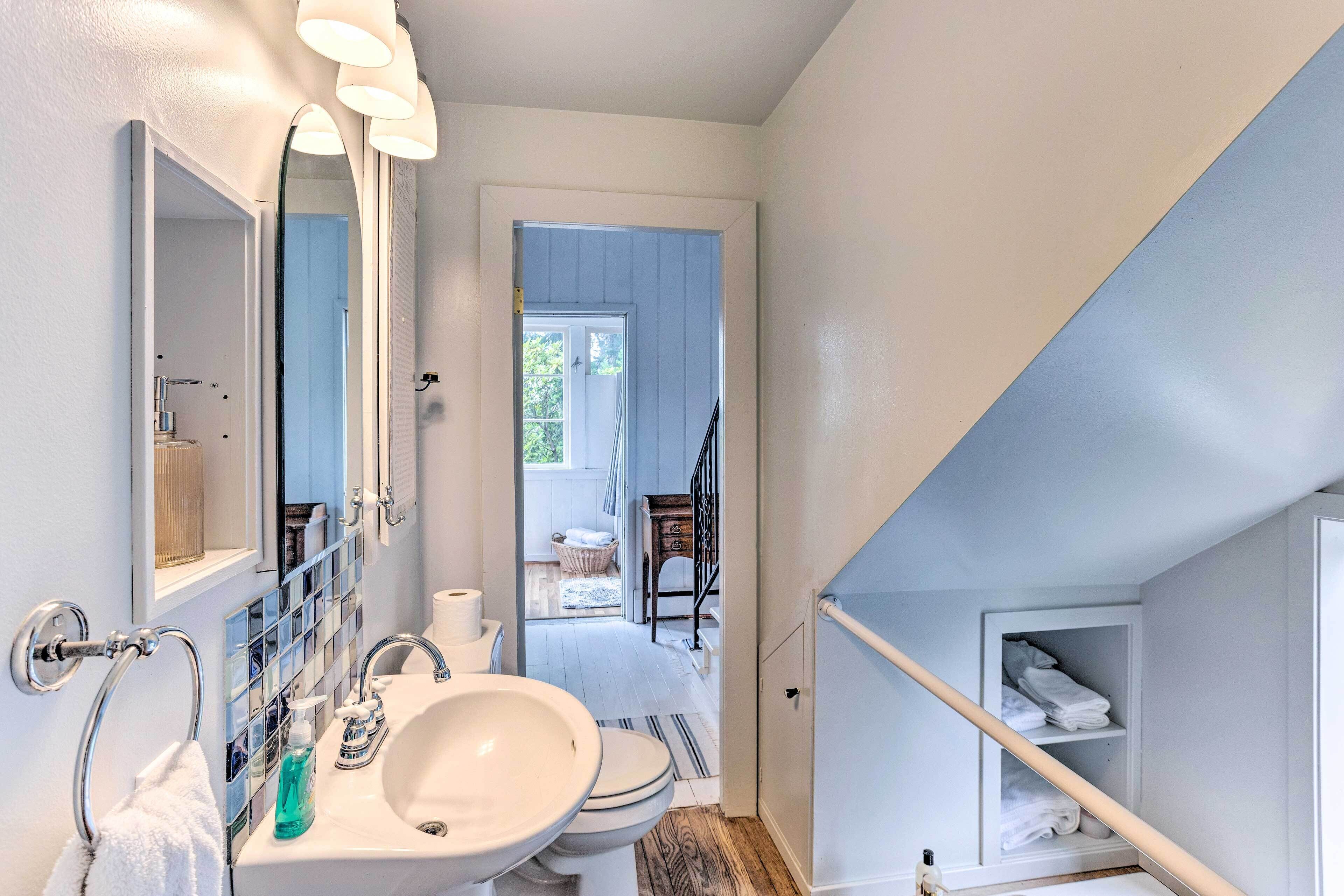 Ein Badezimmer mit Waschbecken, Spiegel und Handtuchhalter. Eine Tür führt zu einem Balkon mit Blick ins Freie.