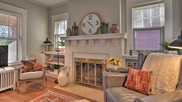 A living room with a fireplace, a clock, and a television. - Vintage Chic Cottage < 1 Mile to UNC Greensboro! (Greensboro)