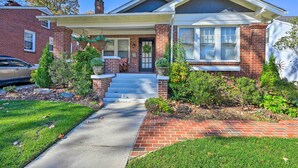 A two-story house with a front porch, brick exterior, and a driveway leading to the entrance. - Vintage Chic Cottage < 1 Mile to UNC Greensboro! (Greensboro)