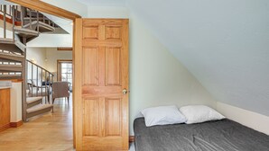 Een slaapkamer met een houten deur, een bed met kussens, een trap en een stoel.