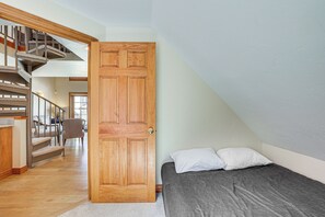 Um quarto com porta de madeira, cama com almofadas, escada e uma cadeira.