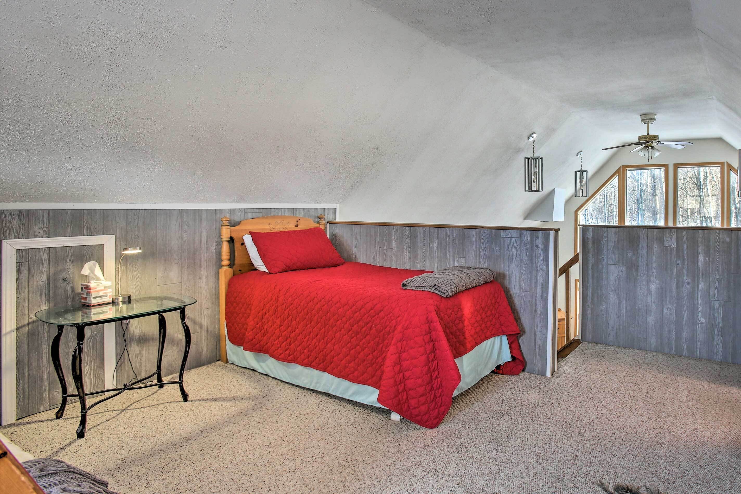 A bedroom with a bed, a small table, a ceiling fan, and a window.
