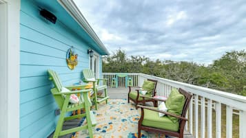 Une terrasse couverte, aménagée avec du mobilier d’extérieur, agrémentée d’une enseigne décorative et offrant une vue sur le paysage environnant.