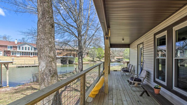 Une terrasse en bois dotée d’une rambarde, de bancs et offrant une vue sur un lac et des bâtiments en arrière-plan.