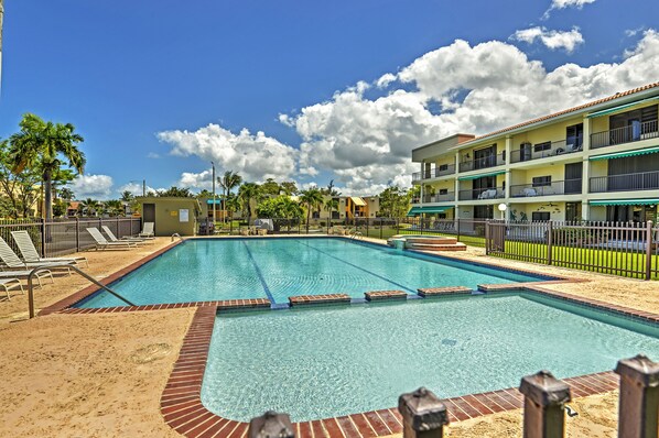 A swimming pool with lounge chairs and a building with balconies in the background.