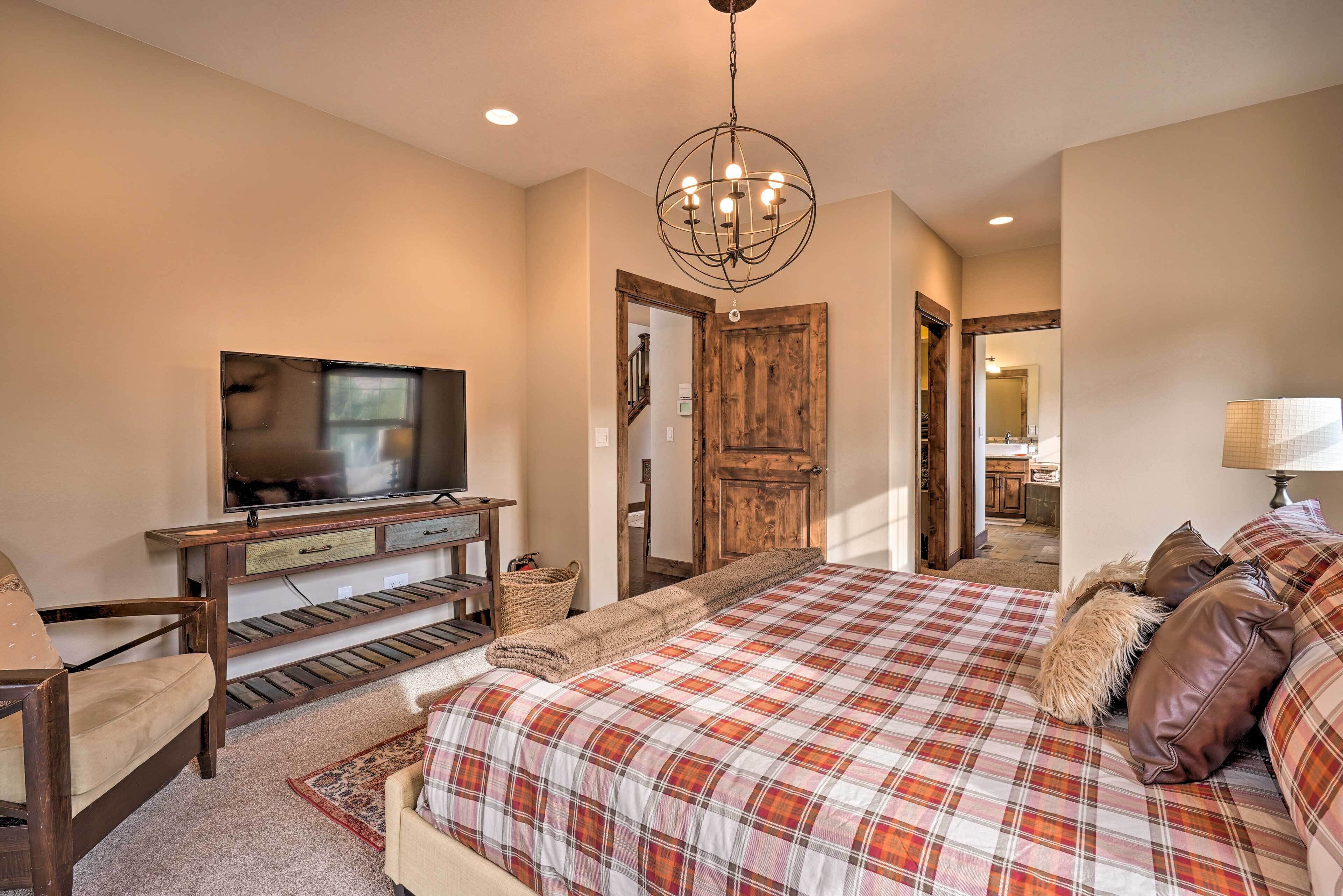 A bedroom with a large bed, a TV, a wooden desk, and a door leading to another room.