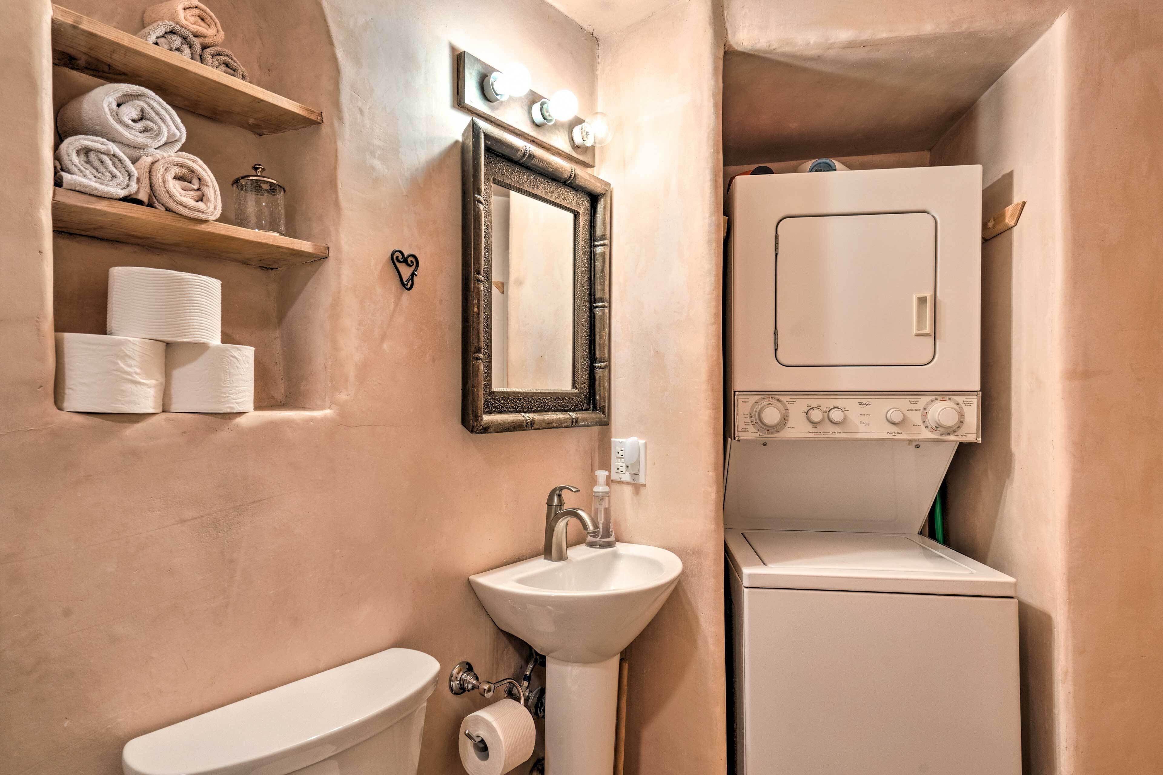 Un bagno funzionale con lavandino, WC e lavatrice. Sono presenti scaffali con asciugamani e articoli da toilette.
