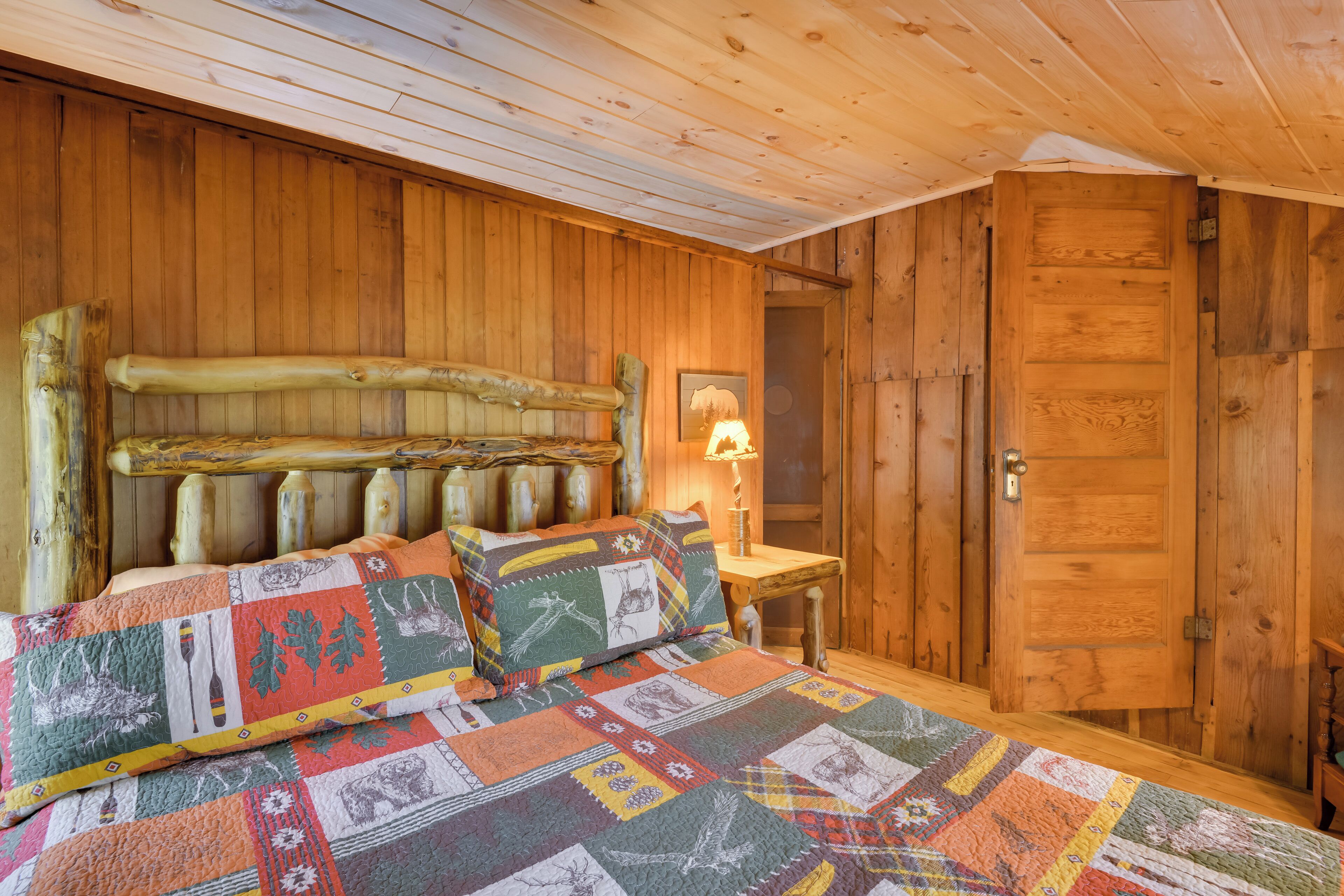 Une chambre dans une cabane en bois, avec un lit, une couette, une tête de lit en bois et une porte.