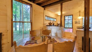 Ein Holzblockhaus mit Essbereich, Stühlen und Küchenzeile, wobei ein Fenster auf den Wald blickt.