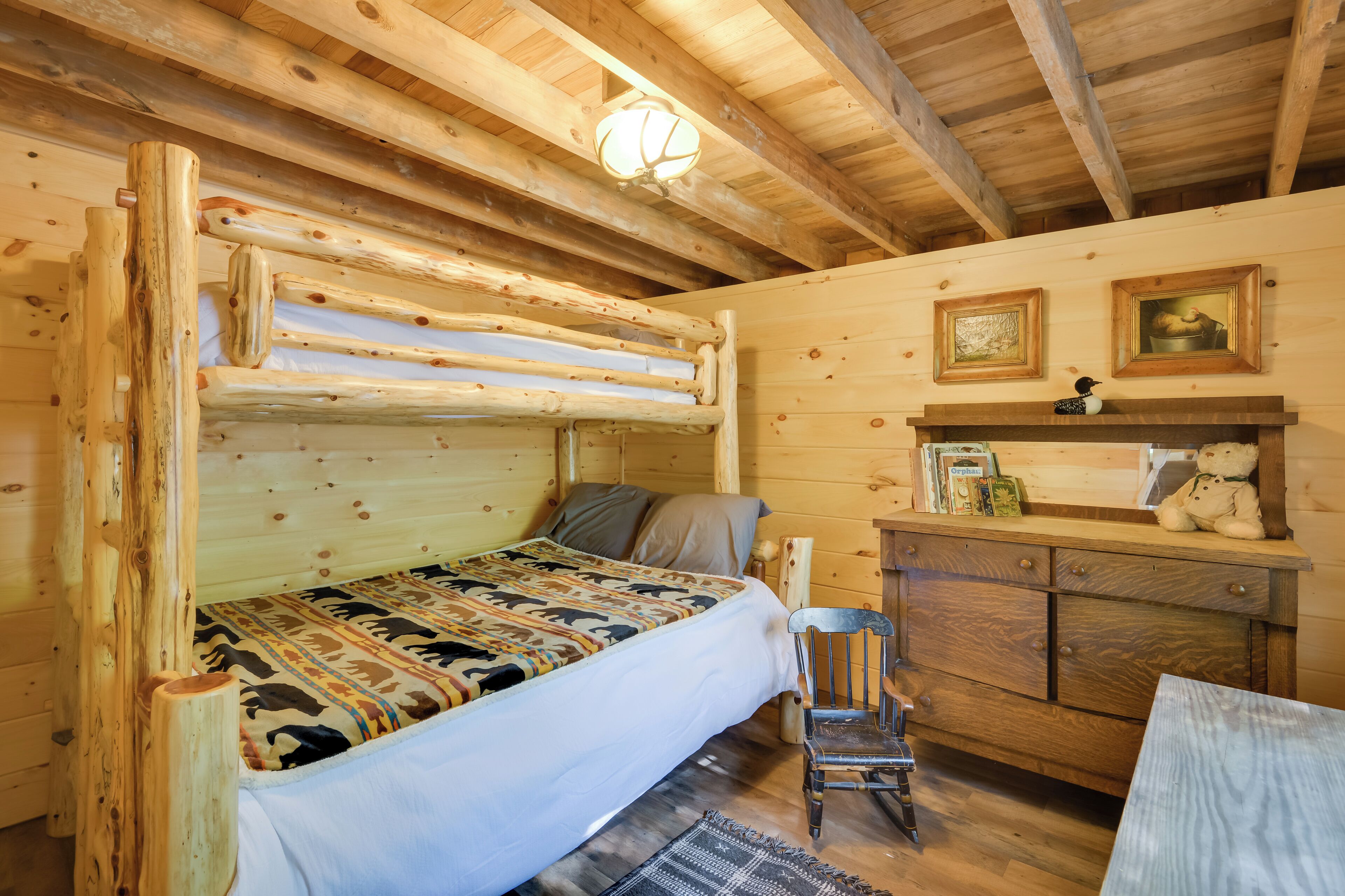 A rustic wooden cabin bedroom with a bunk bed, a small wooden dresser, and a chair.