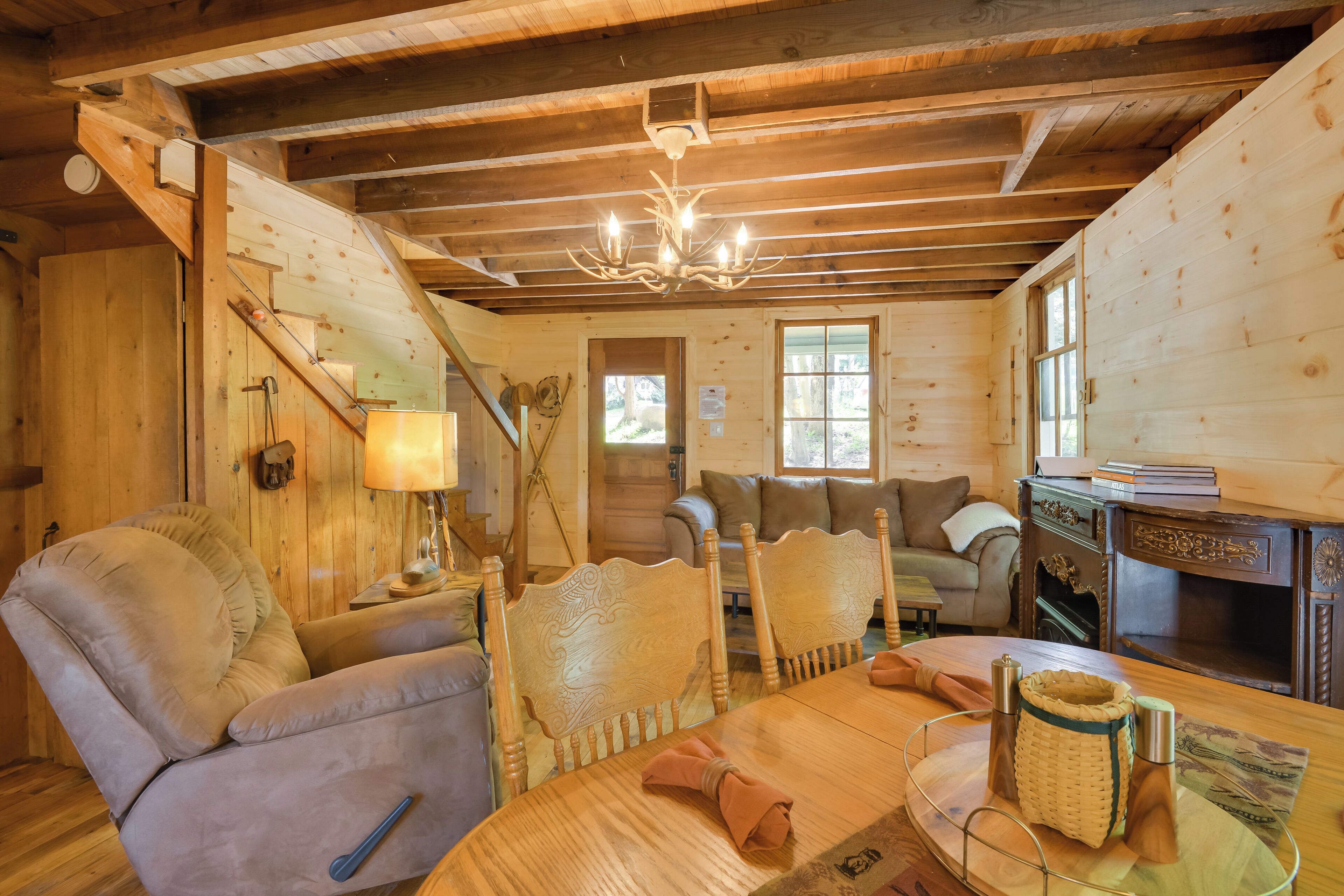 A cozy log cabin interior with a wooden dining table, cushioned chairs, a sofa, and a fireplace.