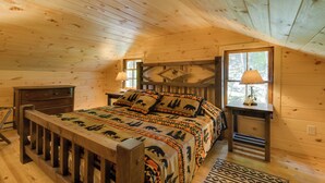 Ein gemütliches Schlafzimmer einer Holzhütte mit einem Bett, einem Nachttisch, einer Kommode und einem Fenster.