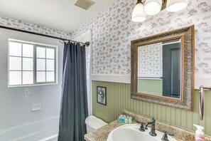A bathroom with a bathtub, a sink with a mirror, and a window with a curtain.