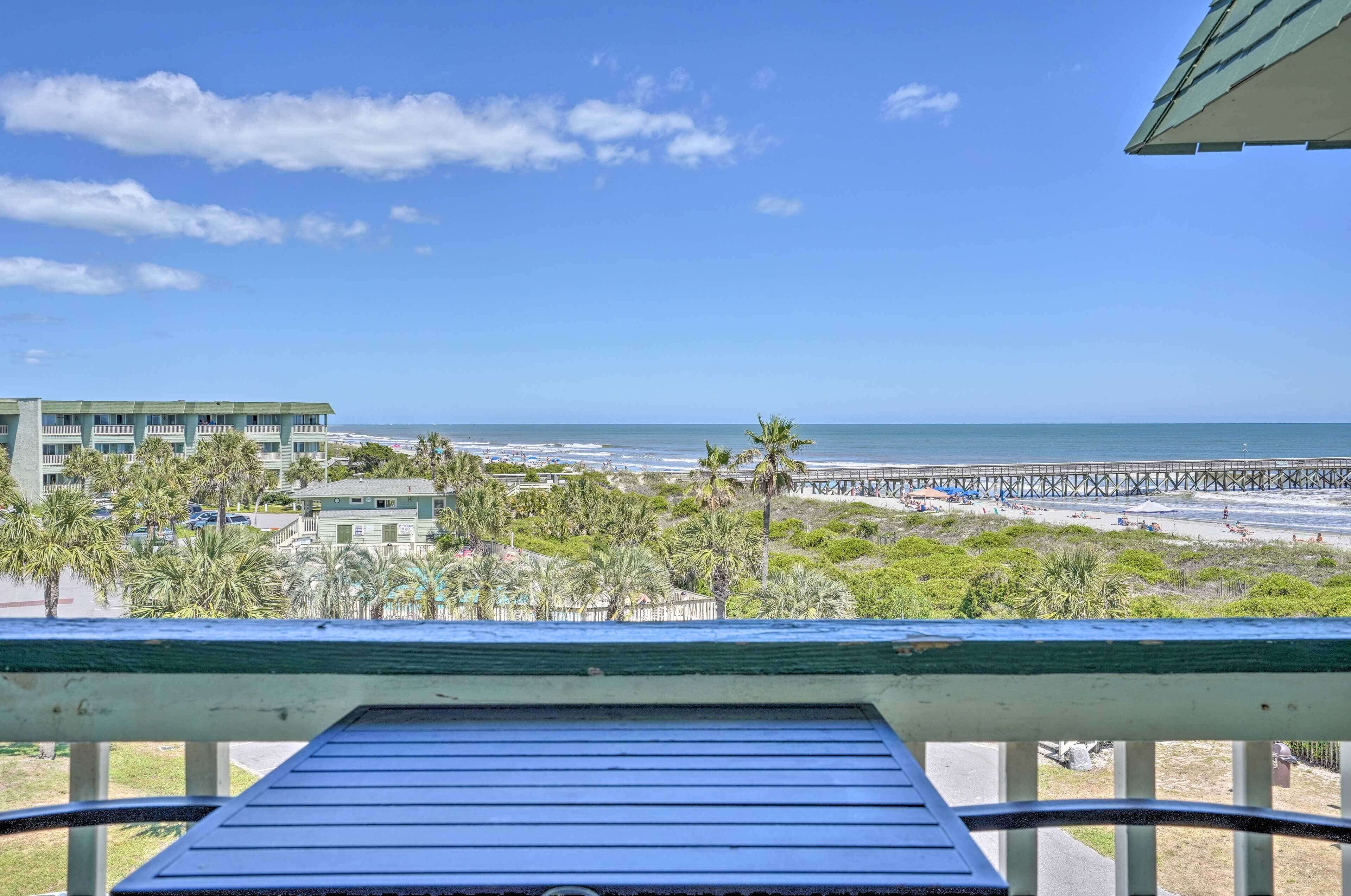 A balcony with a view of the beach, palm trees, and a pier.